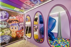 Colorful ball pit and play area inside a purple-themed children's entertainment space with curved walls and oval windows.