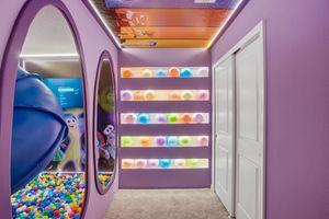 Colorful ball pit room with purple walls and white trim features illuminated LED windows creating a playful atmosphere.