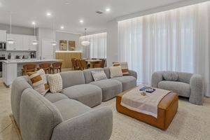 Modern living room features gray sectional sofa, recessed lighting, and wood accent furniture in a bright open space.