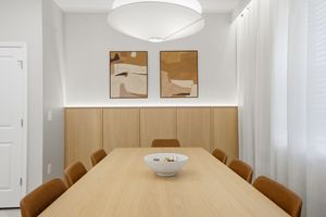 Modern dining room with white pendant light, light wood table, and brown leather chairs against a neutral wall.
