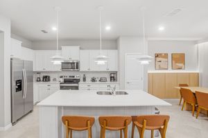 Modern white kitchen with wooden bar stools and recessed lighting showcases clean lines and minimalist design.