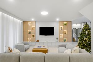 Modern living room with built-in shelving, mounted TV, gray sectional sofa, and decorated Christmas tree in corner.