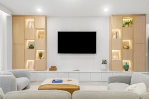 Minimalist living room featuring wall-mounted TV flanked by illuminated wooden shelving units and comfortable seating.