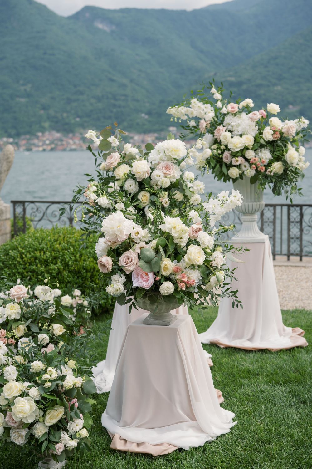 White floral arrangements on pedestals with mountain lake vista in the background.