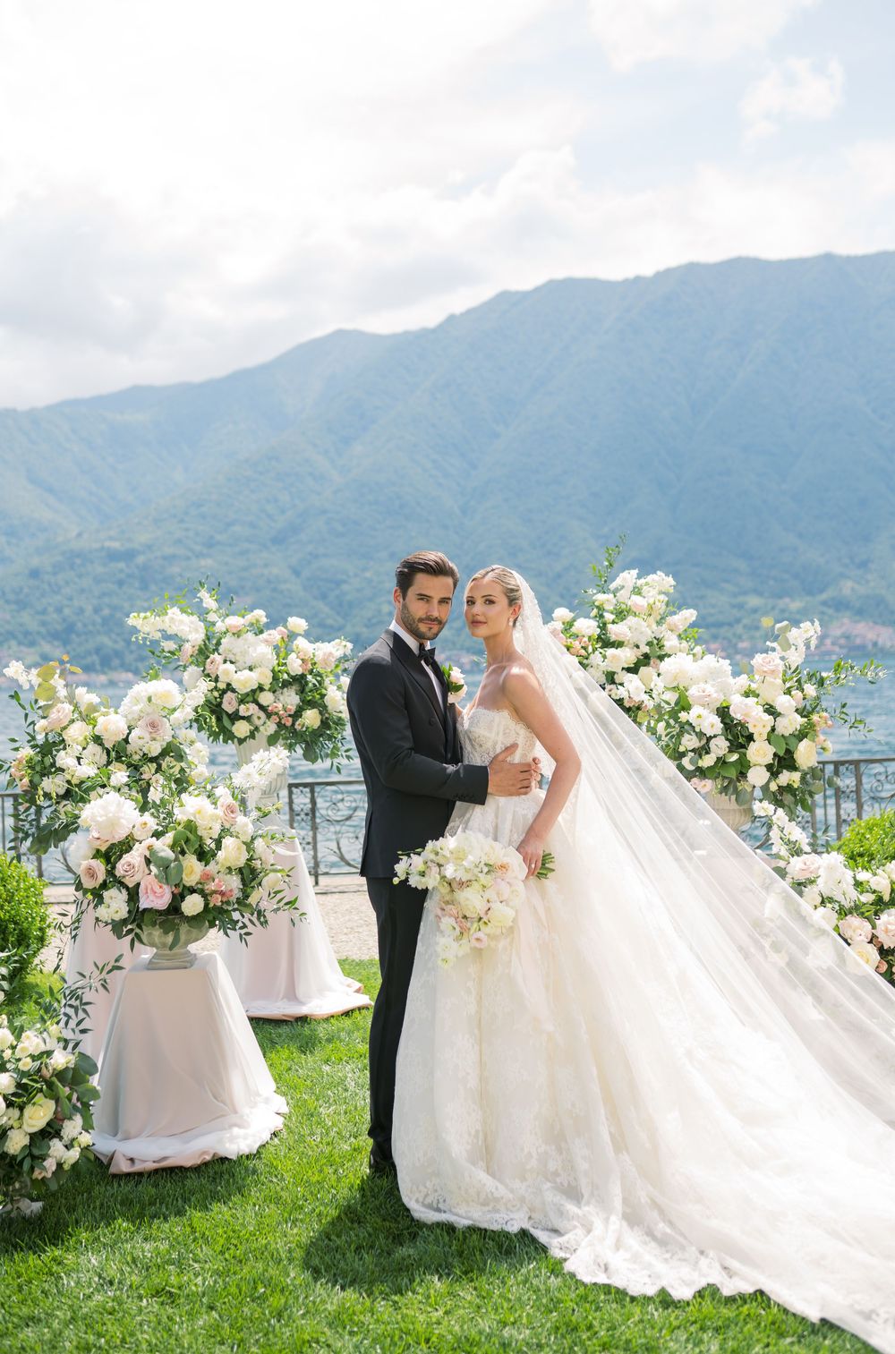 Elegant wedding ceremony with white floral arrangements and mountain lake backdrop.
