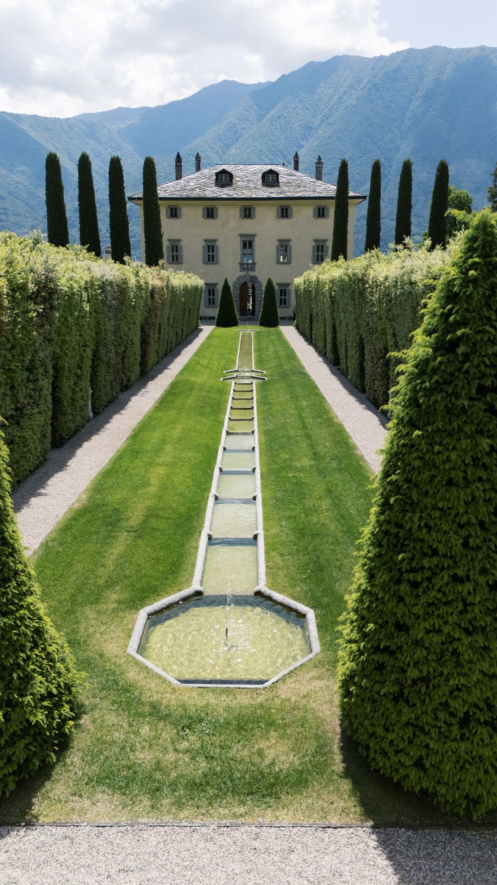 Symmetrical Italian villa garden with water features and cypress trees framing a grand mansion.
