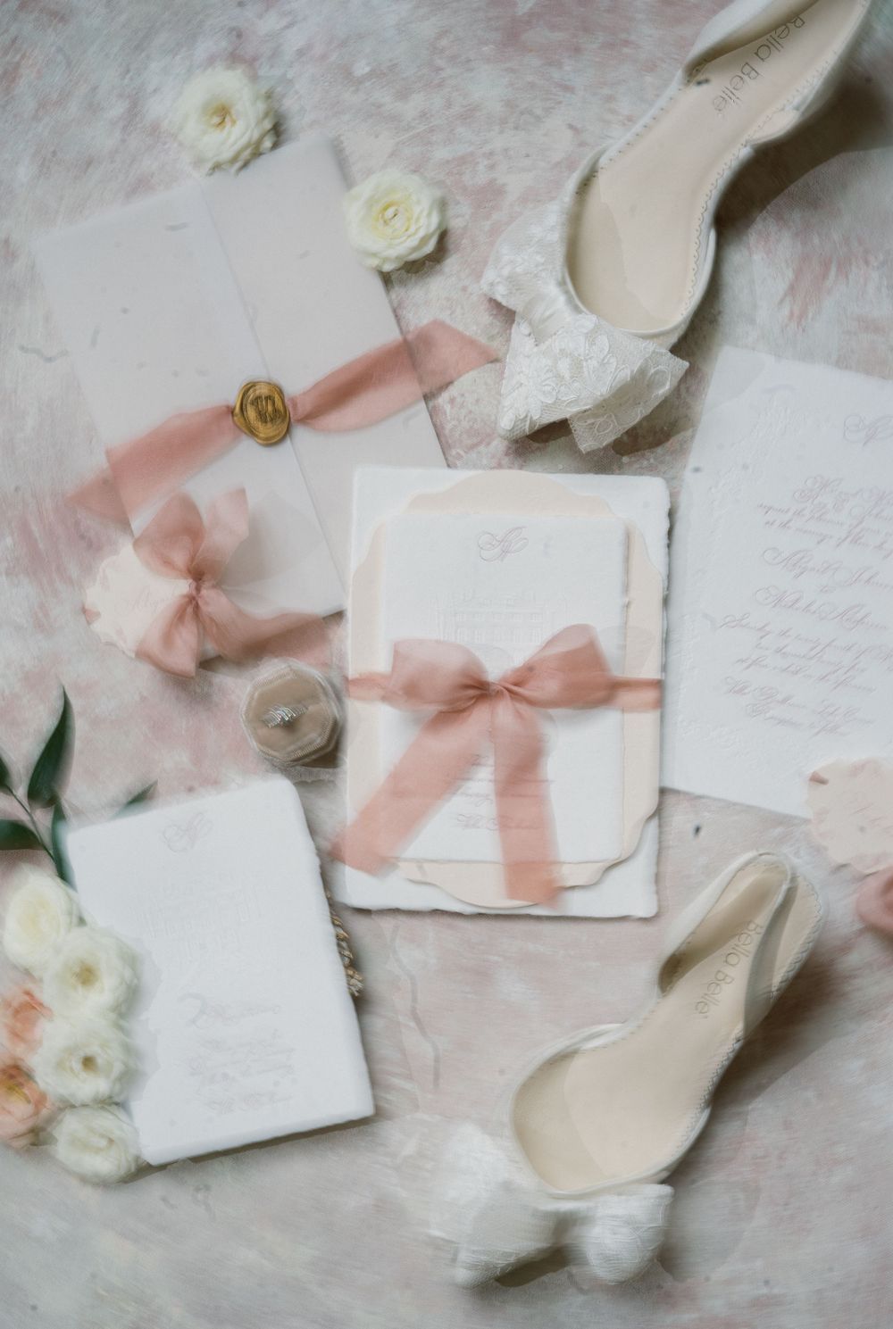 Wedding stationery flat lay with blush pink ribbons and white flowers on marble background.