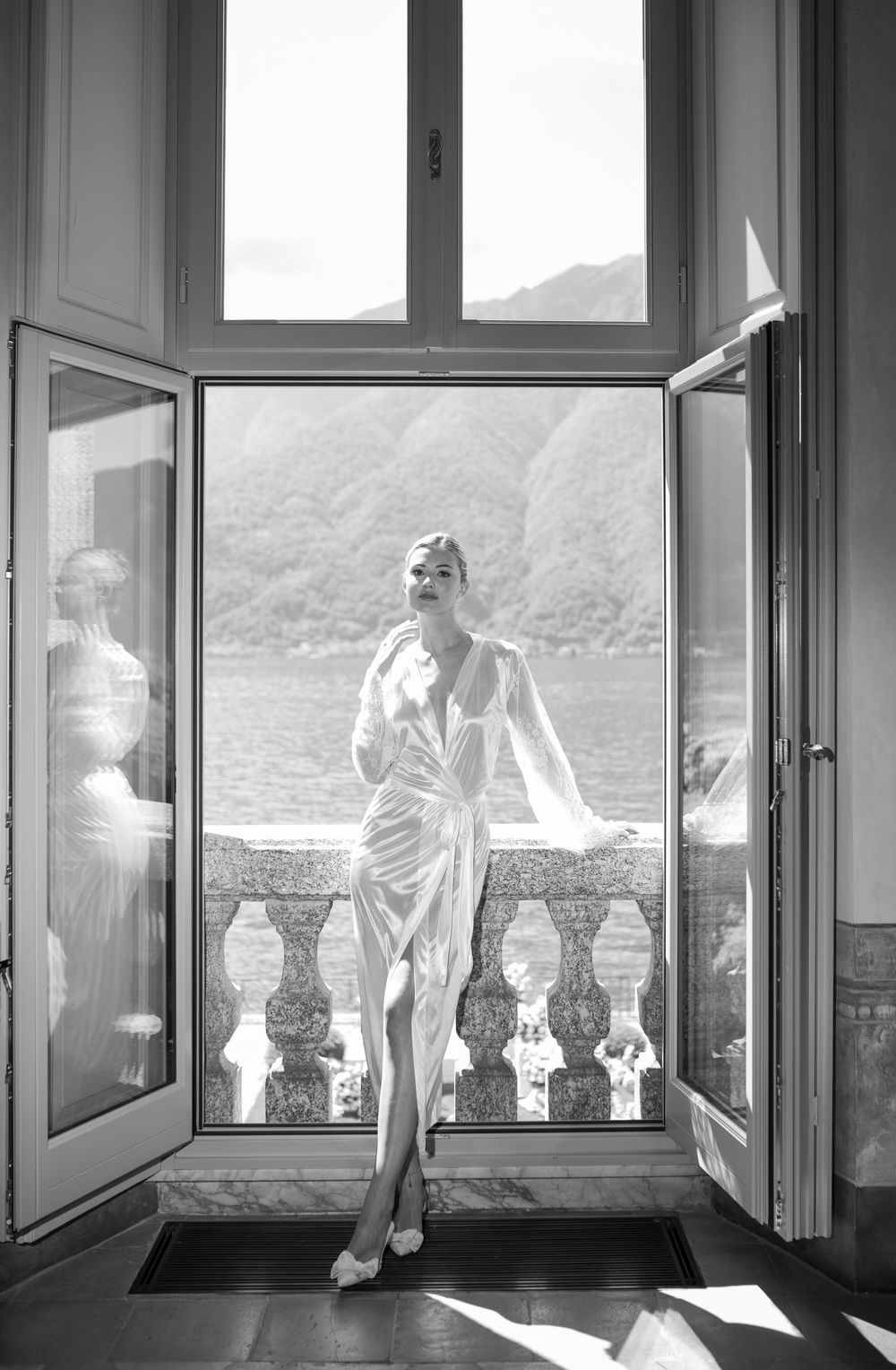 Black and white photograph of a sunlit villa balcony overlooking a lake.