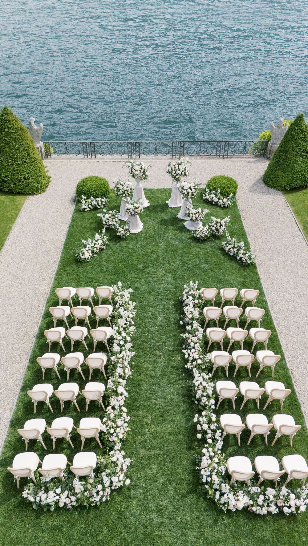 Elegant outdoor wedding ceremony setup with white chairs and floral aisle arrangements overlooking a lake.