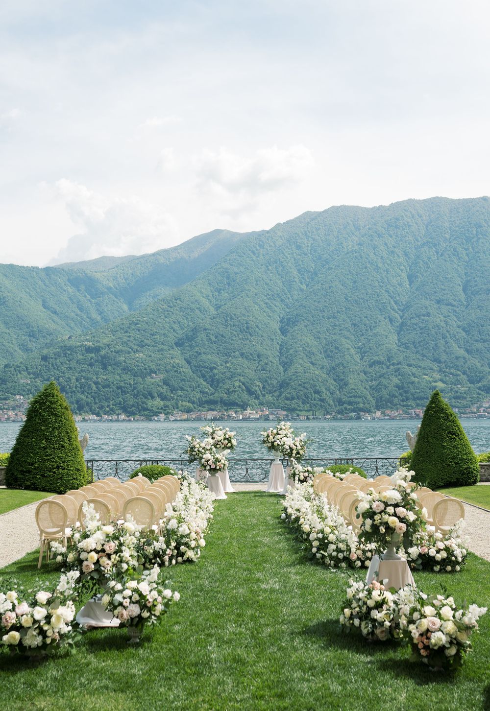 Garden wedding ceremony setup with white chairs and floral decorations against a mountain lake backdrop.