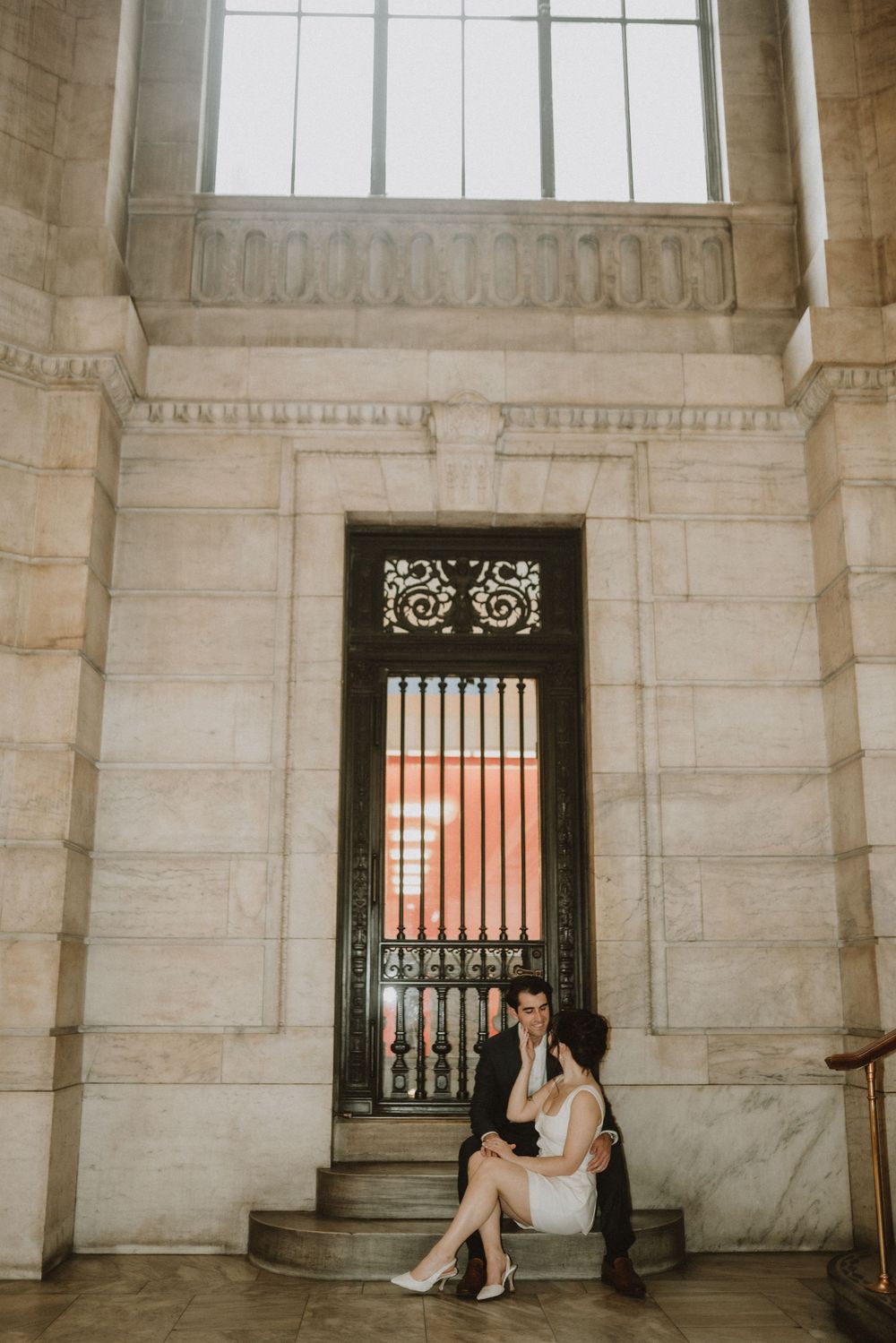 Romantic engagement photo session in an elegant marble building with ornate architectural details and wrought iron gates.