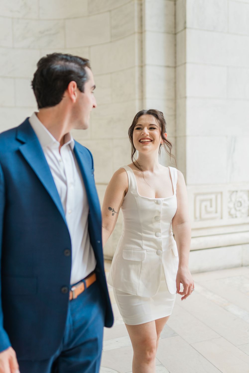 Couple in blue suit and white dress share joyful moment in marble hallway.
