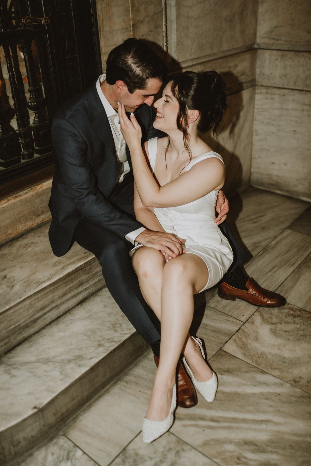 Romantic couple in formal attire share an intimate moment sitting on marble steps.