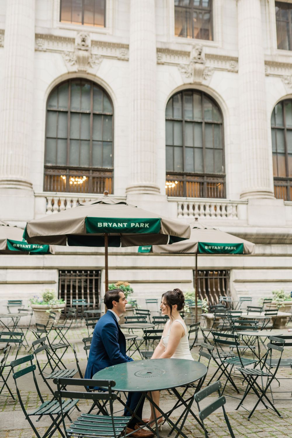 Couple sits at Bryant Park cafe table surrounded by green chairs.