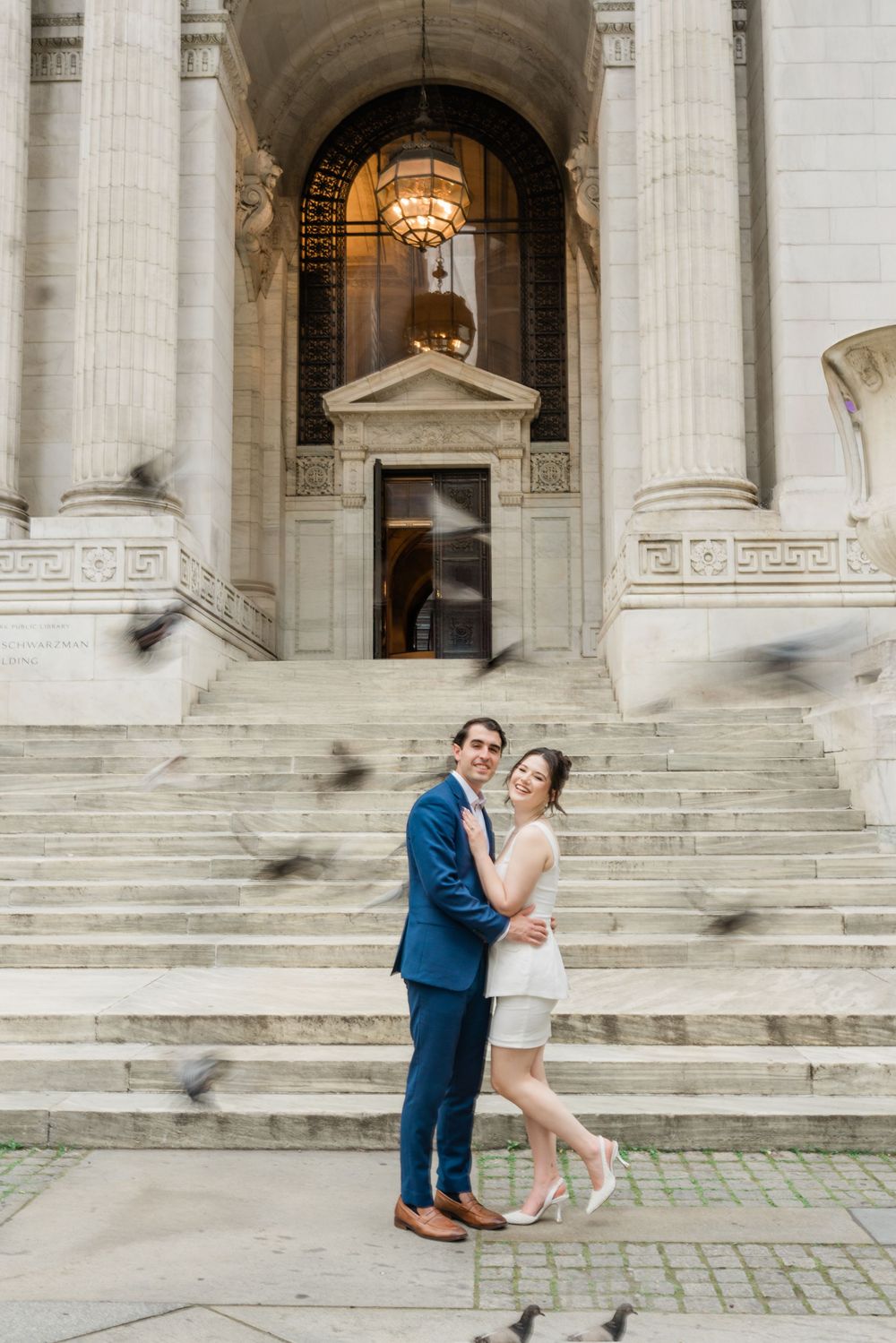 Couple embraces on steps of neoclassical building with grand columns.