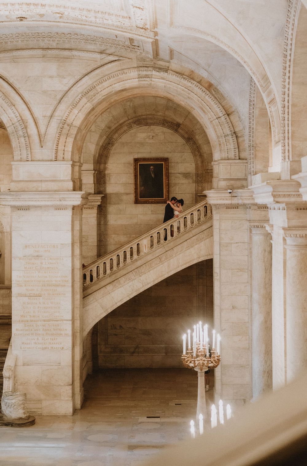 Elegant marble staircase with chandelier and arched architecture in historic building.