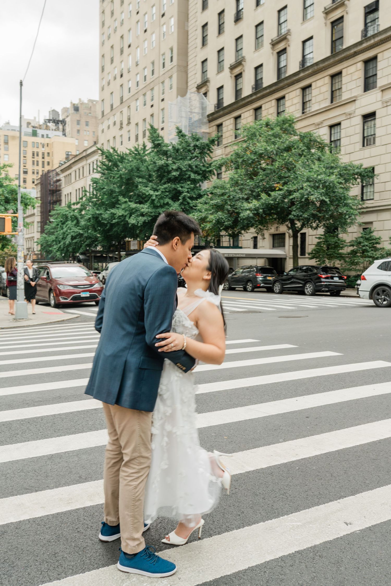 Urban crosswalk scene with tall residential buildings and tree-lined street.