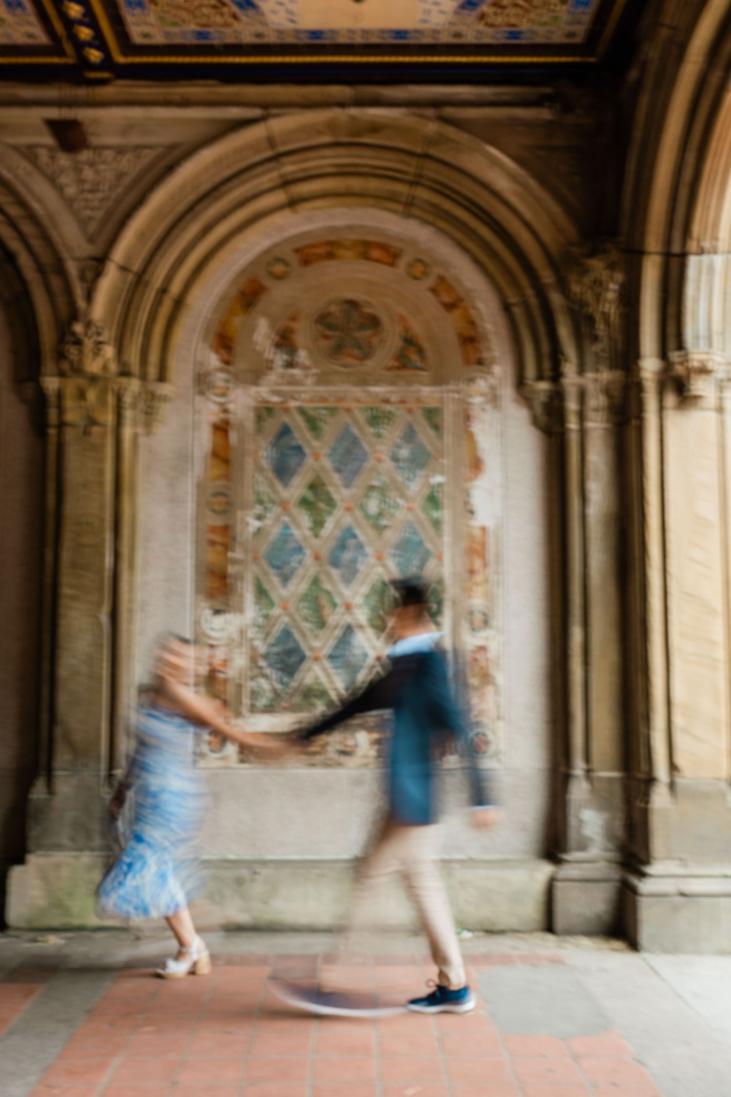 Motion-blurred figures moving through an ornate stone archway with decorative wall patterns.