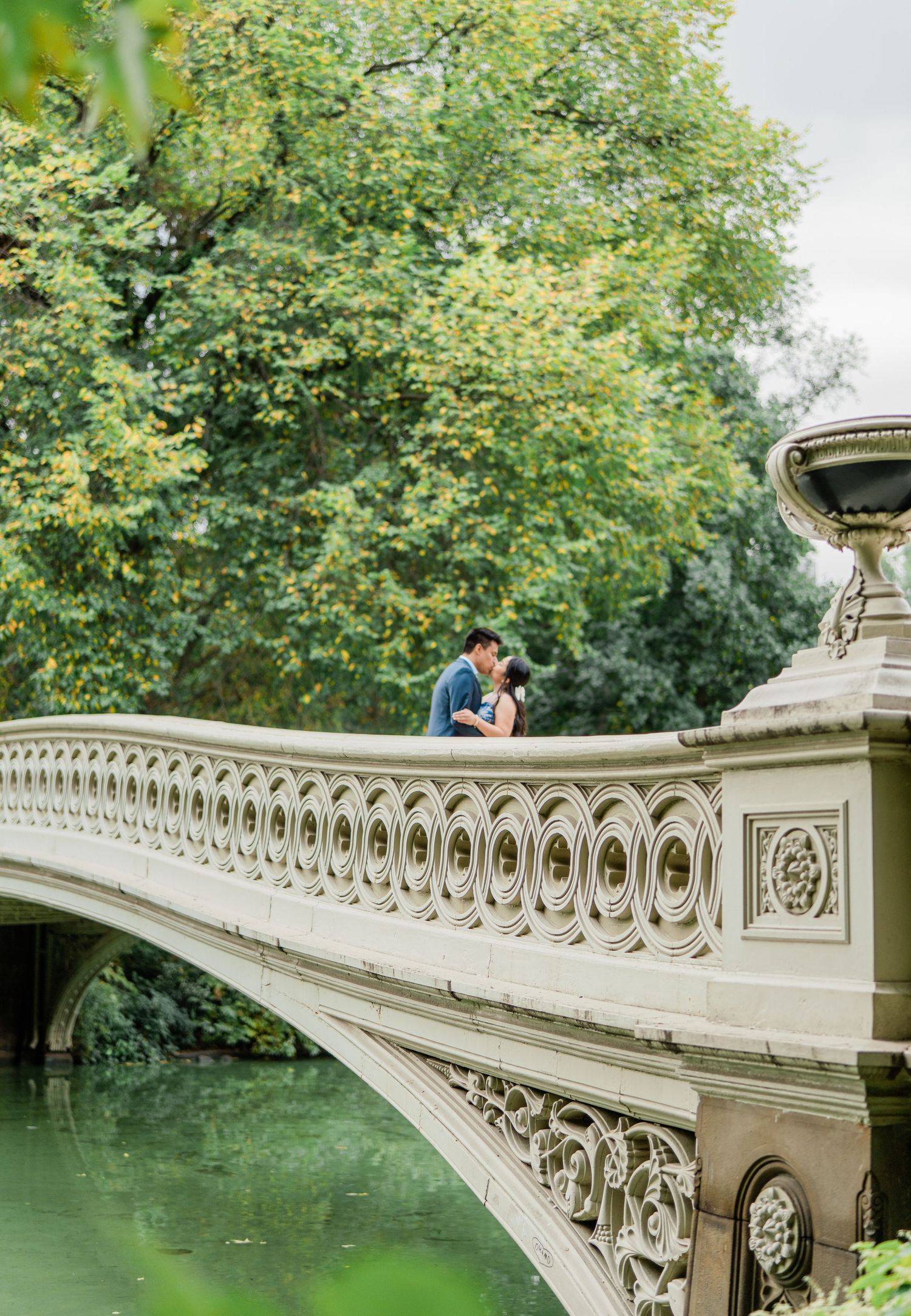 Romantic moment on the ornate Bow Bridge in Central Park with greenery and water below.