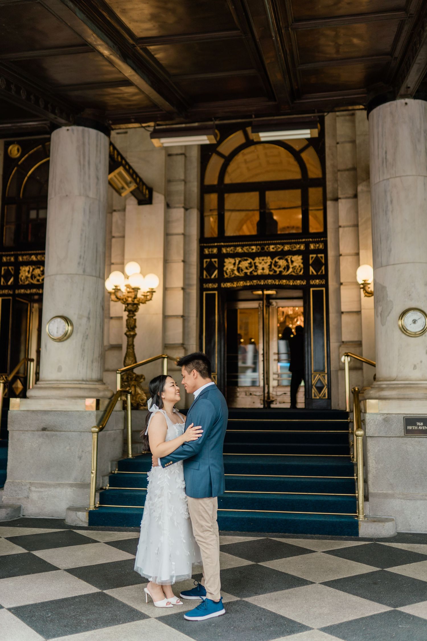 Couple dancing in an elegant lobby with classic columns and checkerboard floor.