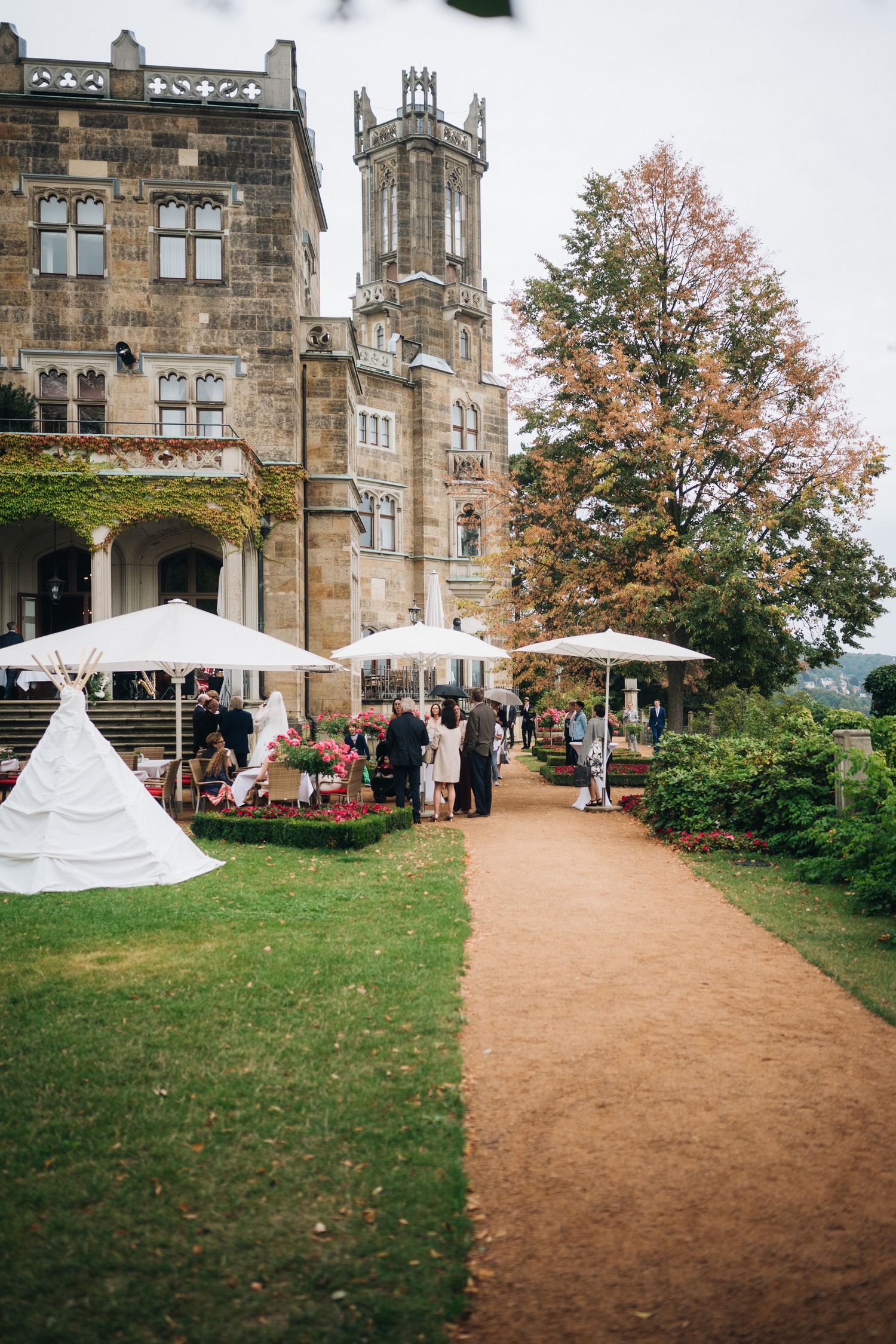 Walkway leading to a Gothic style castle building with autumn trees and white decorative tents on the lawn.