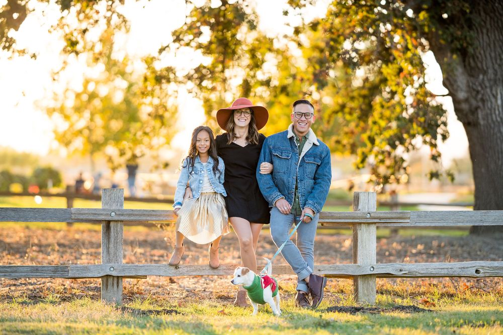 Family poses together at sunset by a wooden fence in a rustic outdoor setting.