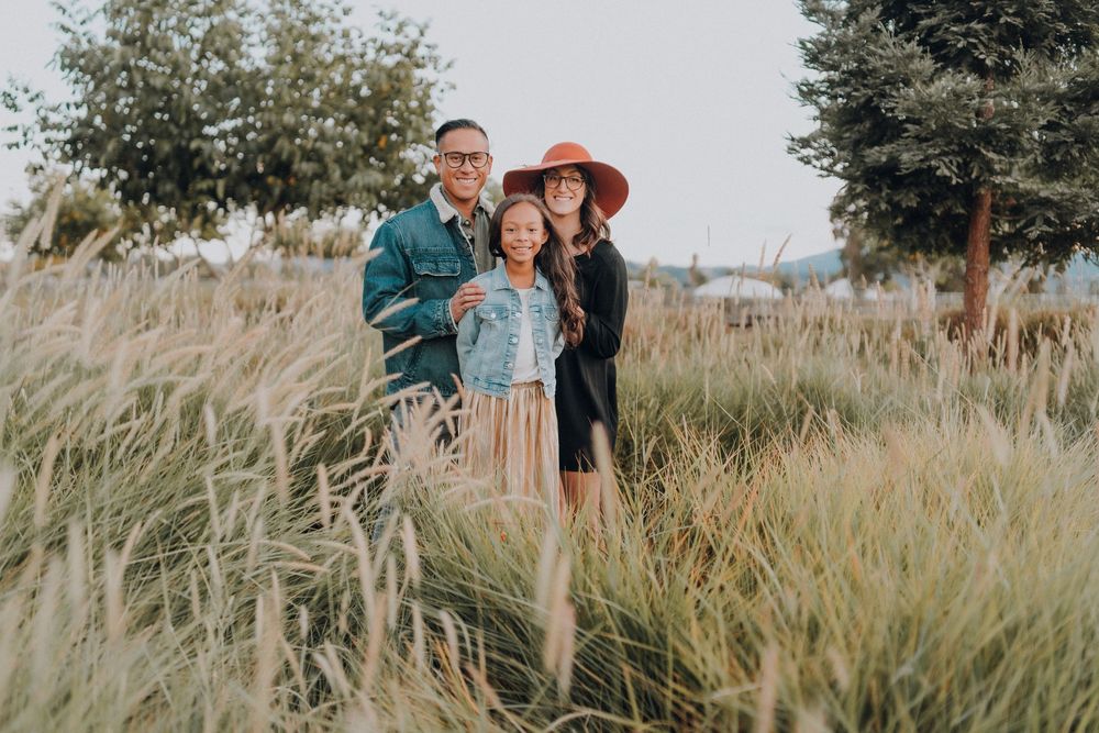 Family stands together in tall grass during golden hour with hats.