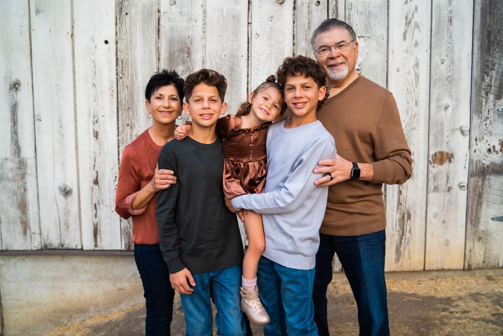 A group of people pose casually against a rustic white wooden fence background for a family photo.