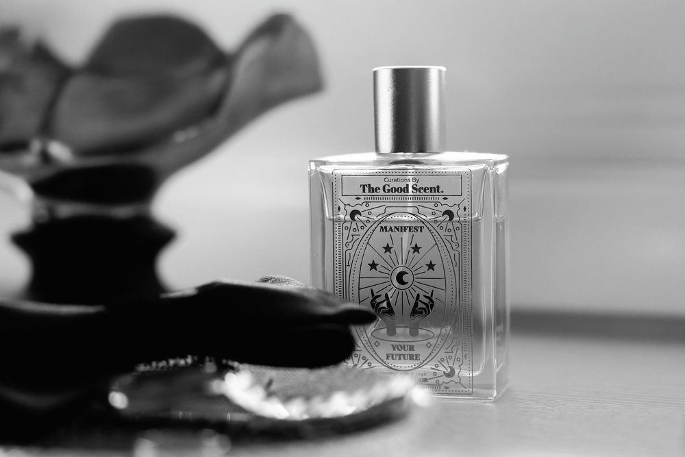 A black and white photograph of a luxury perfume bottle with decorative design alongside dark silhouetted objects.
