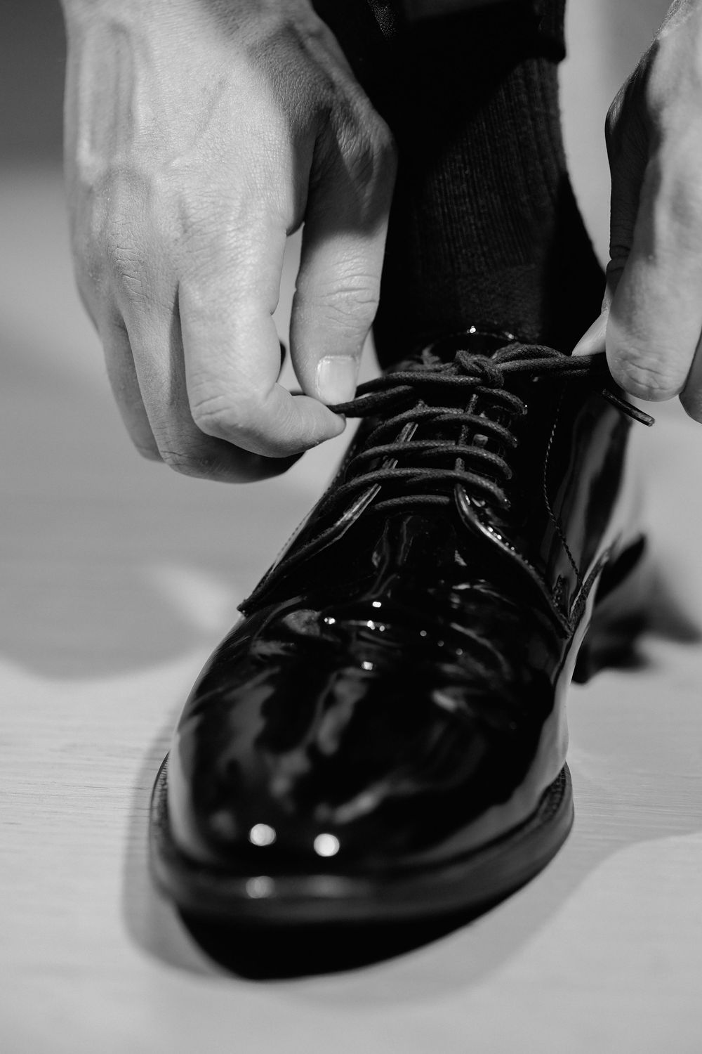 Close-up sequence showing hands tying black patent leather dress shoes in black and white monochrome.