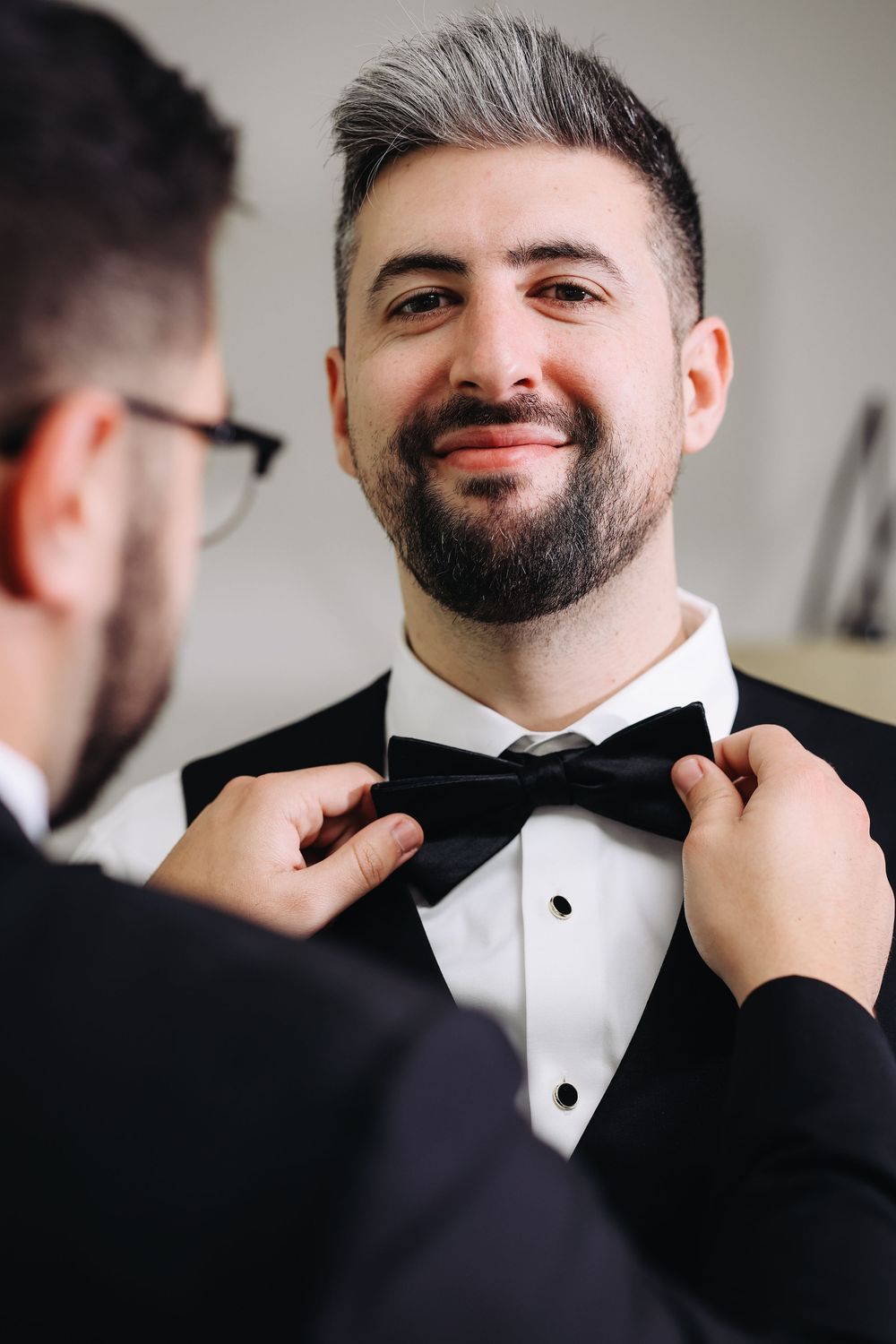 Someone adjusts a black bow tie while getting ready in formalwear before a special event.
