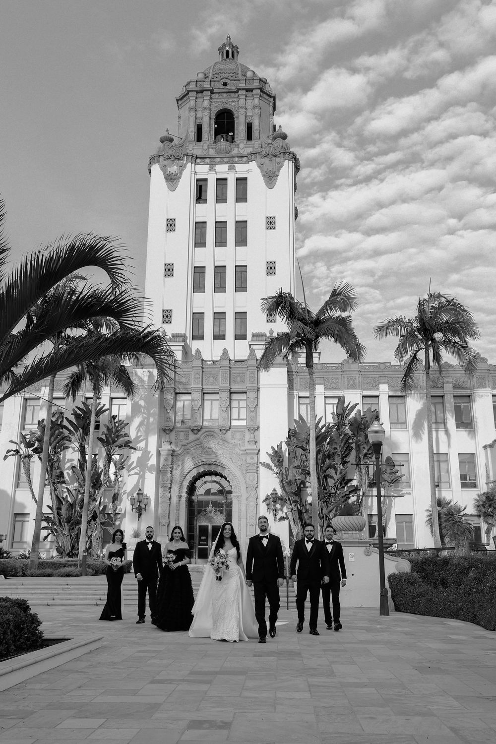 Wedding party poses in front of historic Beverly Hills City Hall with palm trees.