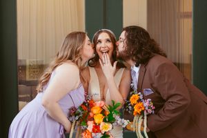 Bridal party members in purple dresses and brown suits share candid laughs during outdoor photo session.
