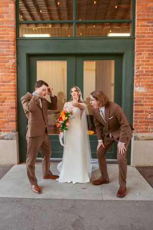 Fun wedding party photo with three people posing playfully outside a brick building.