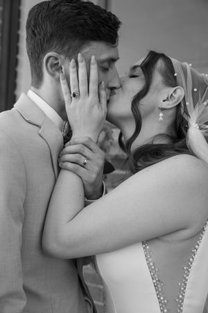 A romantic black and white wedding photo showing a tender kiss between newlyweds wearing rings.
