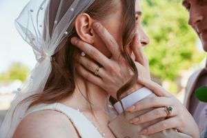 Close-up detail of hands wearing wedding rings during an intimate outdoor wedding ceremony moment.