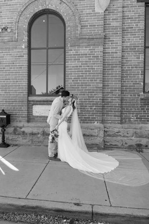 A tender wedding moment captured in black and white outside a brick building with an arched window.
