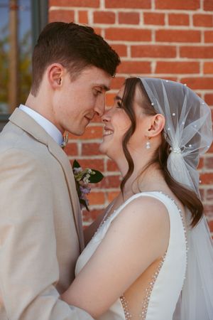 A romantic wedding portrait of a couple in formal attire standing close together against a brick wall.