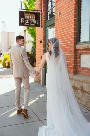 Wedding photography sequence showing couple walking along brick building exterior with flowing veil and dress movement.