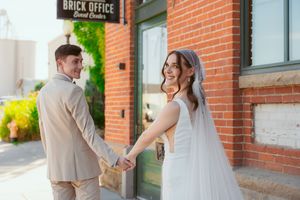 Elegant couple in formal attire standing near a red brick office building with romantic poses for professional photos.