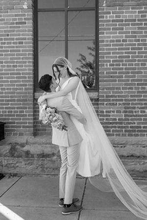 Black and white portrait of wedding couple in intimate embrace by brick building.