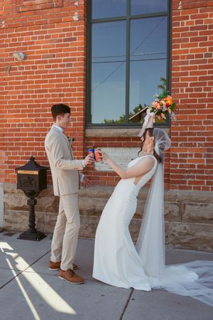A wedding couple is seen in four sequential frames playing hide and seek around a brick building corner.