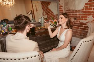 Woman in white dress drinking from a glass in rustic brick interior setting.