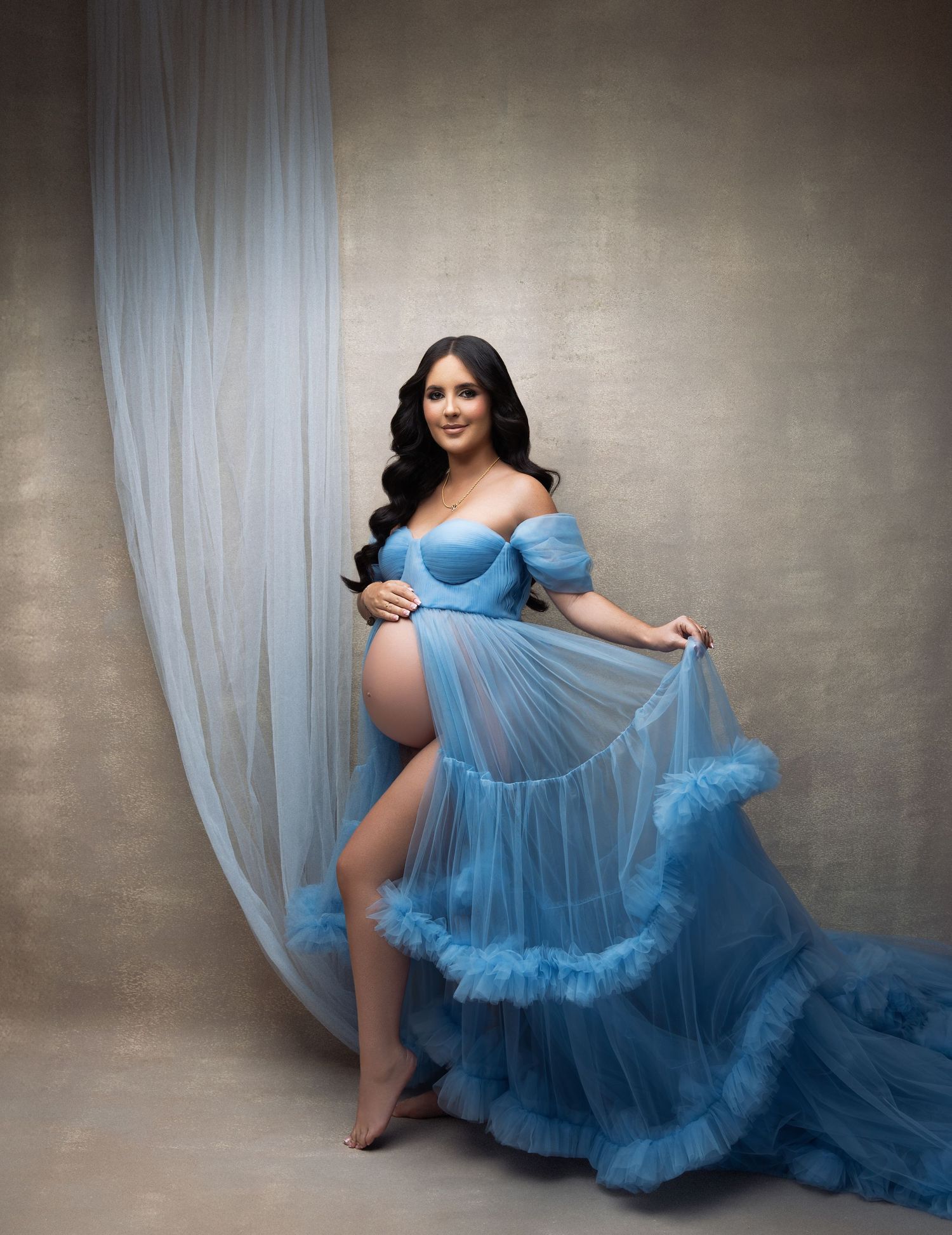 A person in a flowing light blue tulle gown poses gracefully against a textured grey backdrop in a series of moody portraits.