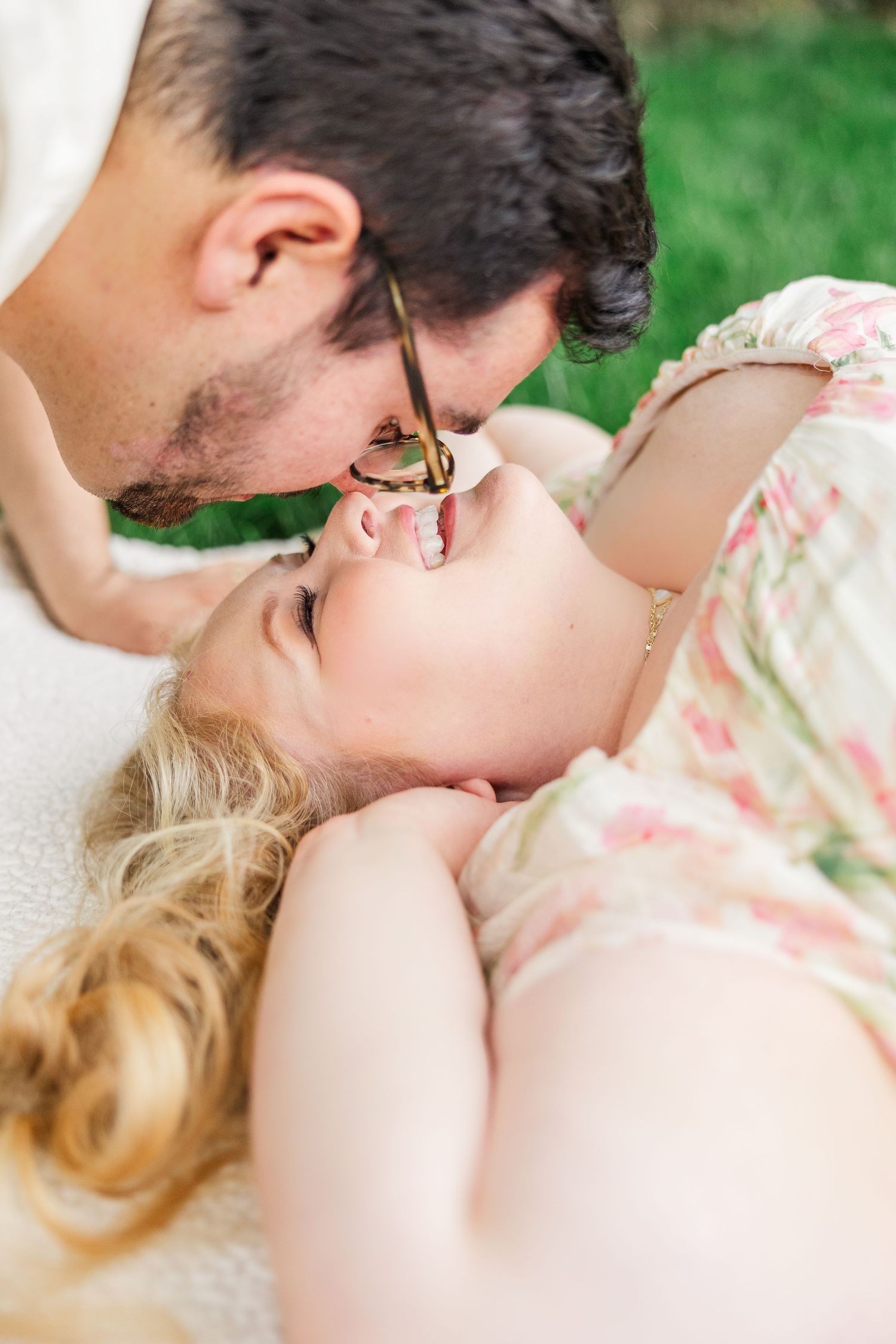 A tender romantic moment captured outdoors with soft natural lighting and floral dress details.