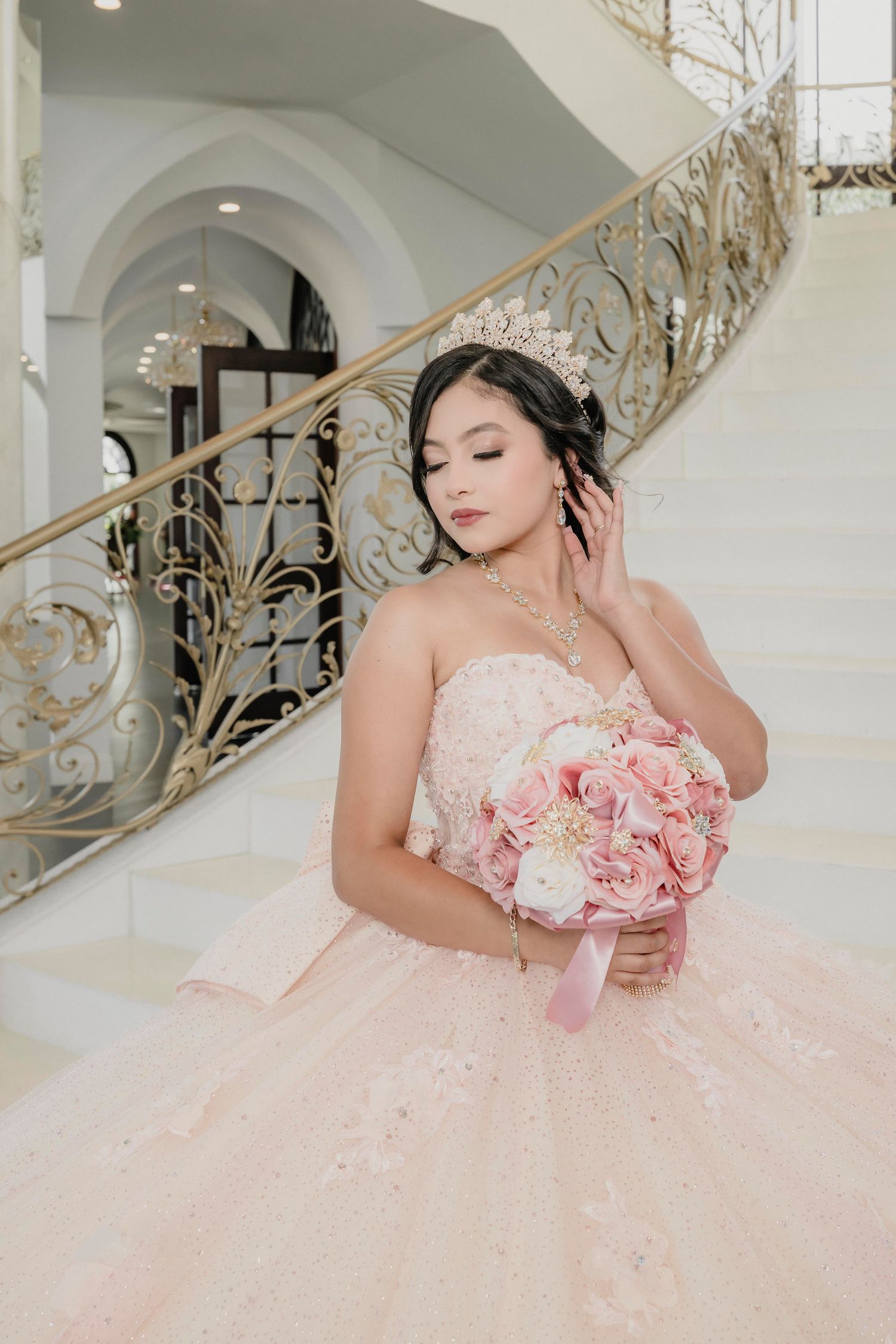 A blush pink ballgown with delicate floral details is photographed in an elegant room with ornate gold railings and chandeliers.