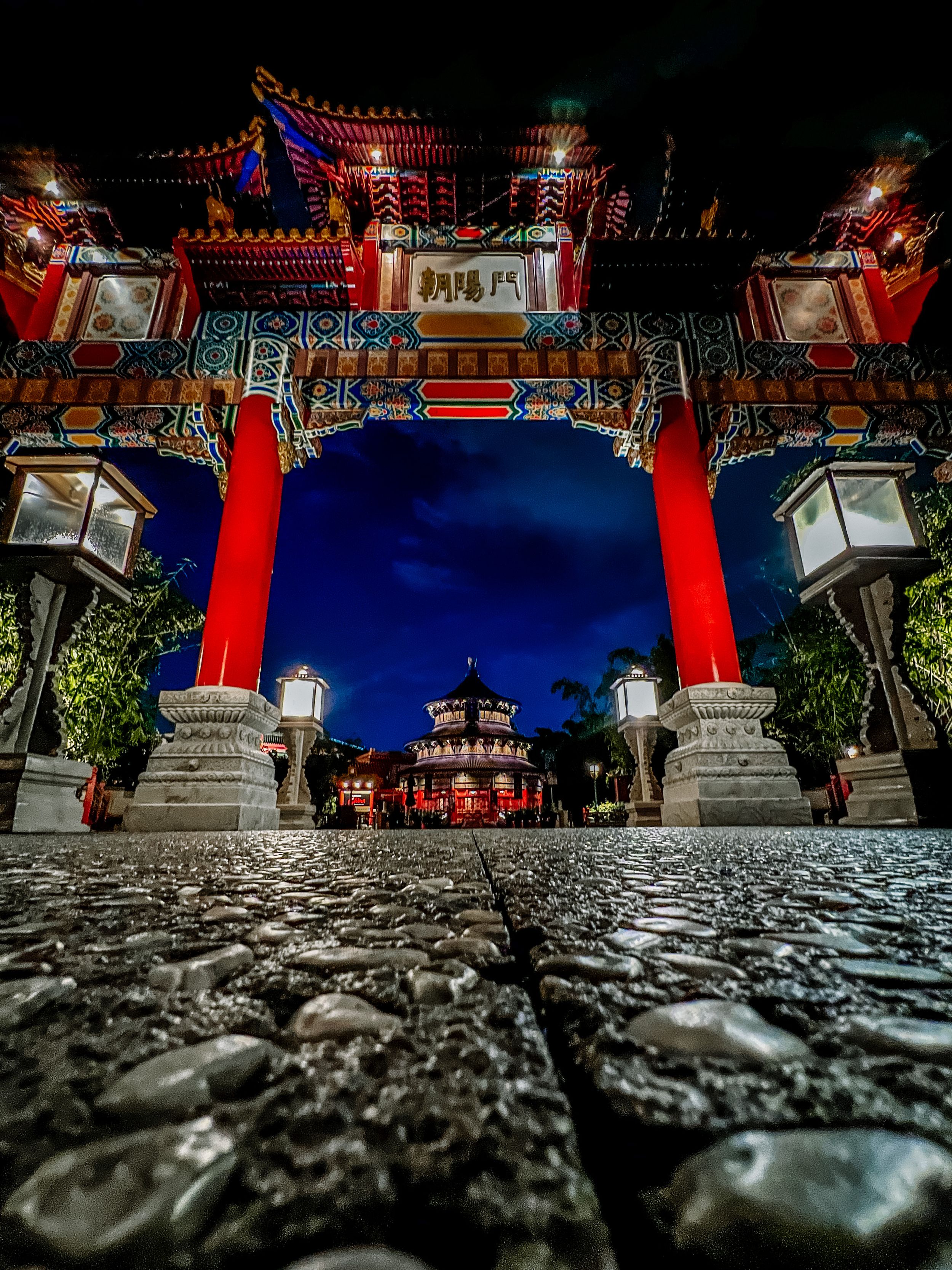 Ornate Chinese temple gate with red pillars and lanterns illuminated at night.