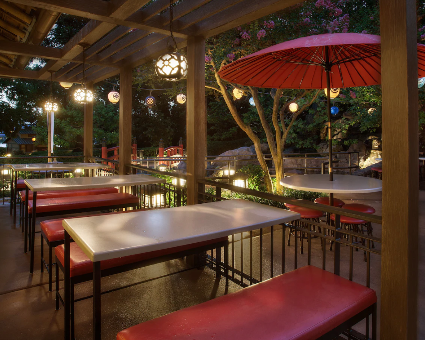 Outdoor restaurant patio with red umbrellas and wooden pergola at dusk.