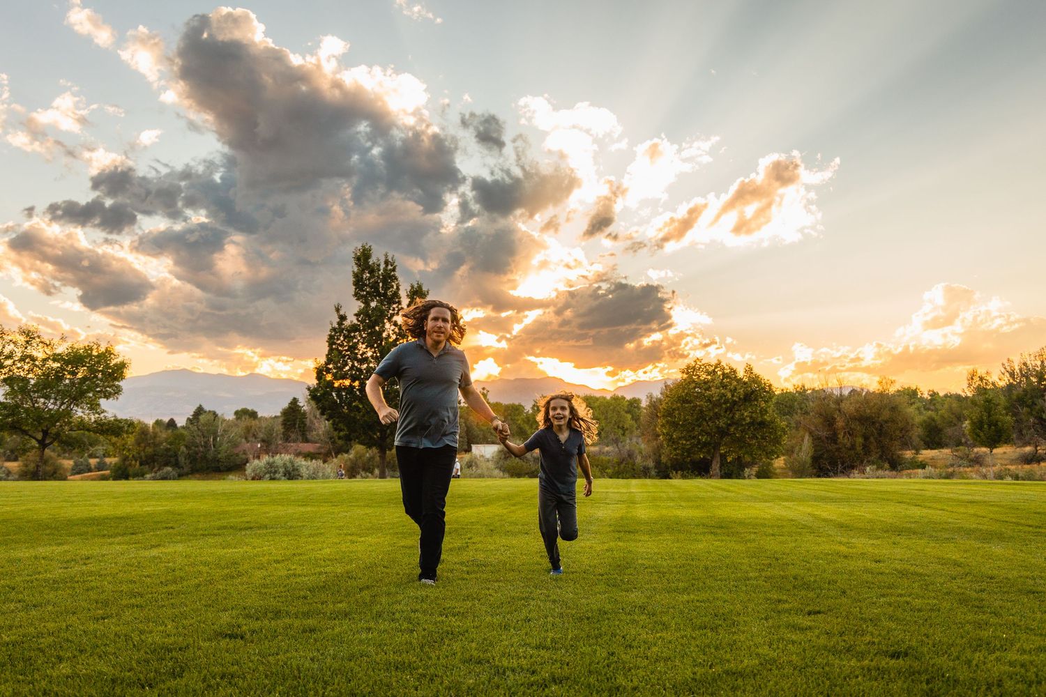 Silhouettes of figures stand together in a grassy meadow against a dramatic sunset sky with wispy clouds.