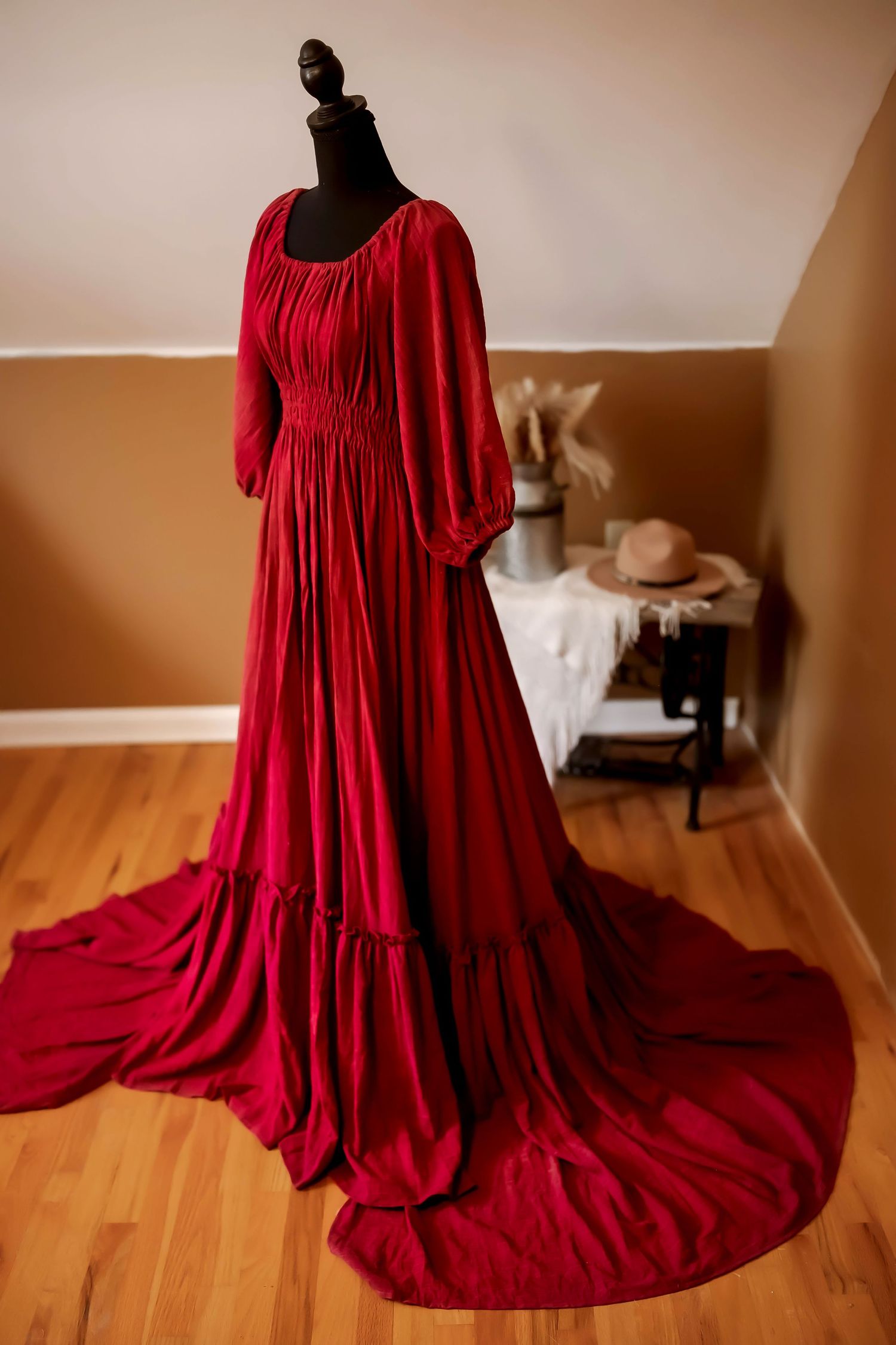 A bright blue cotton dress with puffy sleeves and empire waist hangs on a black mannequin in a room with hardwood floors.